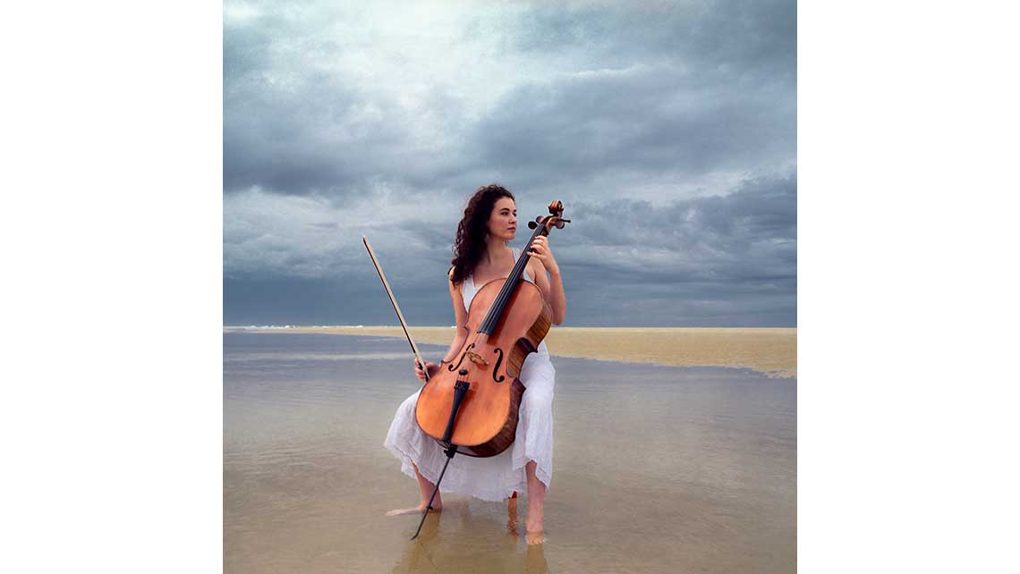 Portrait d'Hélène, élève au Conservatoire de Bordeaux, jouant du violoncelle les pieds dans l'eau sur une plage. © Richard Nourry
