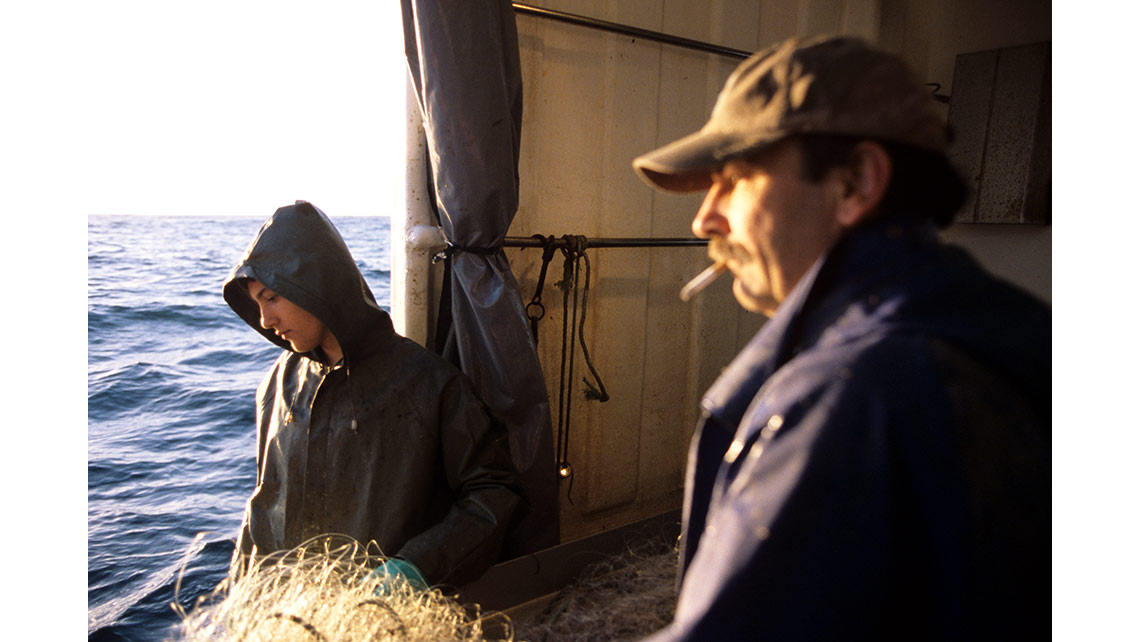 Deux hommes vus de profil pêchent au filet sur un fileyeur d'Arcachon ; © Richard Nourry