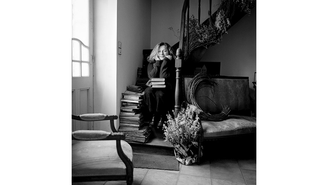 Portrait en noir et blanc de Christine Courrian, vigneronne du Château Gauthier (Médoc - Cru classique d'Yvon Mau), assise sur un escalier à côté d'une pile de livres ; © Richard Nourry
